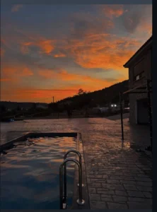 Μαγευτικό ηλιοβασίλεμα με έντονα πορτοκαλί χρώματα να αντανακλώνται στα νερά της πισίνας.